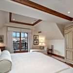 Luxury bedroom with large bed, rustic wardrobe, and mountain view from a window in Beaver Creek, Colorado.