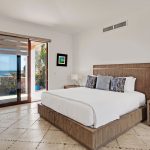 Luxury villa bedroom with ocean view and modern decor, featuring a large bed, wooden furniture, and glass doors opening to a terrace.
