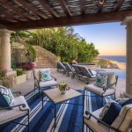 Spacious outdoor patio of a luxury villa in Los Cabos with comfortable seating, decorative pillows, potted plants, and ocean view.