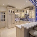 Luxurious kitchen with blue and white tile accents, marble countertops, beige cabinetry, and modern appliances.