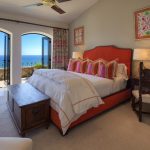 Luxury bedroom with ocean view, featuring a vibrant orange bed, colorful pillows, and a wooden desk with an ornate chair.