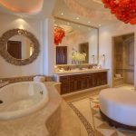 Luxurious bathroom with a large oval bathtub, ornate mirror, wooden cabinetry, and red glass chandeliers in a villa rental in Los Cabos, Mexico.