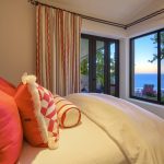 Bedroom with colorful pillows and curtains, overlooking a balcony and ocean view.