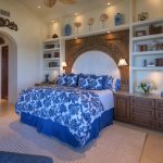 Elegant bedroom with ornate headboard, blue and white bedding, and built-in shelves with decorative items and books.