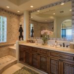 Luxurious bathroom with double sinks, large decorative mirror, and intricate tile work, featuring a window with glass blocks and elegant lighting.