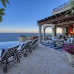 Luxury villa terrace overlooking an infinity pool and ocean, with seating areas and flowering plants.