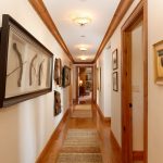 A well-lit hallway in a luxury villa with wooden floors, art pieces, and framed paintings on the walls.
