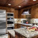 Luxurious kitchen with wooden cabinetry, stainless steel appliances, and a granite island topped with a charcuterie board and wine glasses.