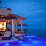 Luxury villa with illuminated pool and ocean view at dusk in Los Cabos, Mexico.