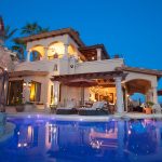Luxury villa with stone and stucco exterior, pool, and ocean view at dusk.