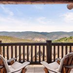 Two wooden chairs on a balcony overlooking a mountainous landscape.
