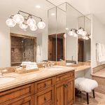 Luxurious bathroom with dual sinks, a large mirror, wooden cabinets, plush stool, and a corner bathtub with decorative accents.
