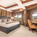 Cozy bedroom in a luxury villa with rustic wooden walls, a plush bed, and a scenic mountain view through large windows.