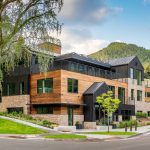 Modern mountain lodge with wood and brick exterior, surrounded by lush greenery and scenic views.