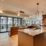 Modern kitchen interior with large island, pendant lights, and a view of snowy mountains through floor-to-ceiling windows.