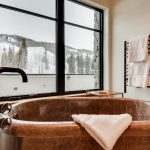 Luxurious bathroom with a marble bathtub, mountain view through large windows, and towel rack.