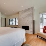 Luxurious bedroom with a modern fireplace, large windows showing snowy mountain views, and elegant decor including a chair with a deer head pillow.