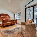 Luxury villa bedroom with wooden bed, plush rug, and balcony view of snowy mountains in Vail, Colorado.