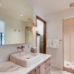 Modern bathroom with a wall-mounted sink, marble countertop, large mirror, and glass-enclosed shower.