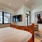 Bedroom interior with a wooden bed, large windows showcasing a snowy mountain view, a mounted TV, and a horse portrait on the wall.