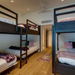 A room with two sets of bunk beds, adorned with fluffy blankets and pillows, and a colorful rug on a wooden floor.