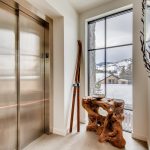 Elevator area with wooden skis and a rustic wooden table near a large window overlooking snowy mountains.