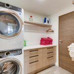 Laundry room with stacked washer and dryer, wooden cabinets, and shelves holding towels and cleaning supplies.
