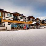 A luxury villa surrounded by snowy mountains in Vail, Colorado, with a collection of skis and snowboards outside.