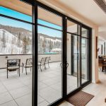 View from inside a luxury villa looking out to a balcony with seating, overlooking snow-covered mountains and trees.