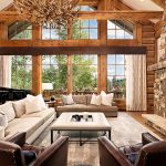 Luxurious living room with large windows, comfortable seating, stone fireplace, and antler chandelier.