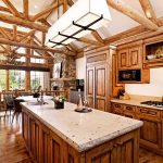 Luxurious kitchen with wooden beams and large windows overlooking a forested mountain view.