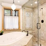 Luxurious bathroom with a large soaking tub and a glass-enclosed shower, featuring elegant stone tile work and a window with checkered curtains.