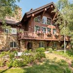 A luxurious mountain villa with large windows and a stone exterior, surrounded by lush greenery and trees in Beaver Creek, Colorado.