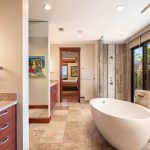 Luxurious bathroom with freestanding bathtub, large windows with garden view, and wooden cabinetry.