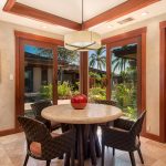 Dining area with a round table, wicker chairs, and large sliding doors overlooking a lush garden with palm trees.