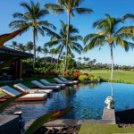 Infinity pool with lounge chairs, surrounded by palm trees and tropical landscape, overlooking a golf course.