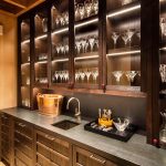Luxurious home bar with a countertop, sink, wine cooler, and glassware cabinets.
