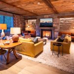 Luxurious living room in a villa with a fireplace, comfortable seating, wooden ceiling, and large window with a forest view.