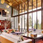Luxurious living room in a villa with large windows, comfortable sofas, decorative lamps, and a rustic wooden ceiling, surrounded by natural scenery.