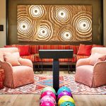 Colorful and cozy living area with patterned rug, armchairs, vibrant pillows, and artistic wall decoration, featuring bowling balls on a wooden floor.