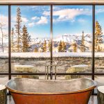 A luxurious bathroom with a freestanding tub and large windows overlooking a snowy mountain landscape.