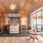 Luxurious bedroom with elegant furnishings, large windows overlooking a snowy landscape, featuring a four-poster bed, plush seating, wooden cabinetry, and a decorative chandelier.