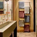 Luxurious bathroom with decorative tiles, a modern rectangular sink, and a towel rack holding several colored towels.
