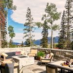 Outdoor patio with comfortable seating and fire pit, surrounded by tall trees and mountain views.