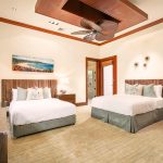 Elegant bedroom with two beds, tropical-themed decor, ceiling fan, and large windows.