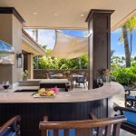 Luxury outdoor patio with a bar, wine glasses, and tropical decor overlooking lush greenery and palm trees.