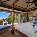 Luxury villa bedroom with ocean view, featuring elegant furniture, patterned bedding, and an outdoor seating area overlooking tropical plants and the beach.