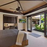 Luxury villa bedroom with large glass doors opening to a tropical garden view in Hawaii.