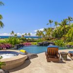 Luxury villa patio with sun loungers, jacuzzi, and pool overlooking tropical gardens and ocean in Hawaii.