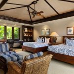 Luxury villa bedroom with two double beds, tropical decor, wicker chairs, and a view of lush greenery through large windows.